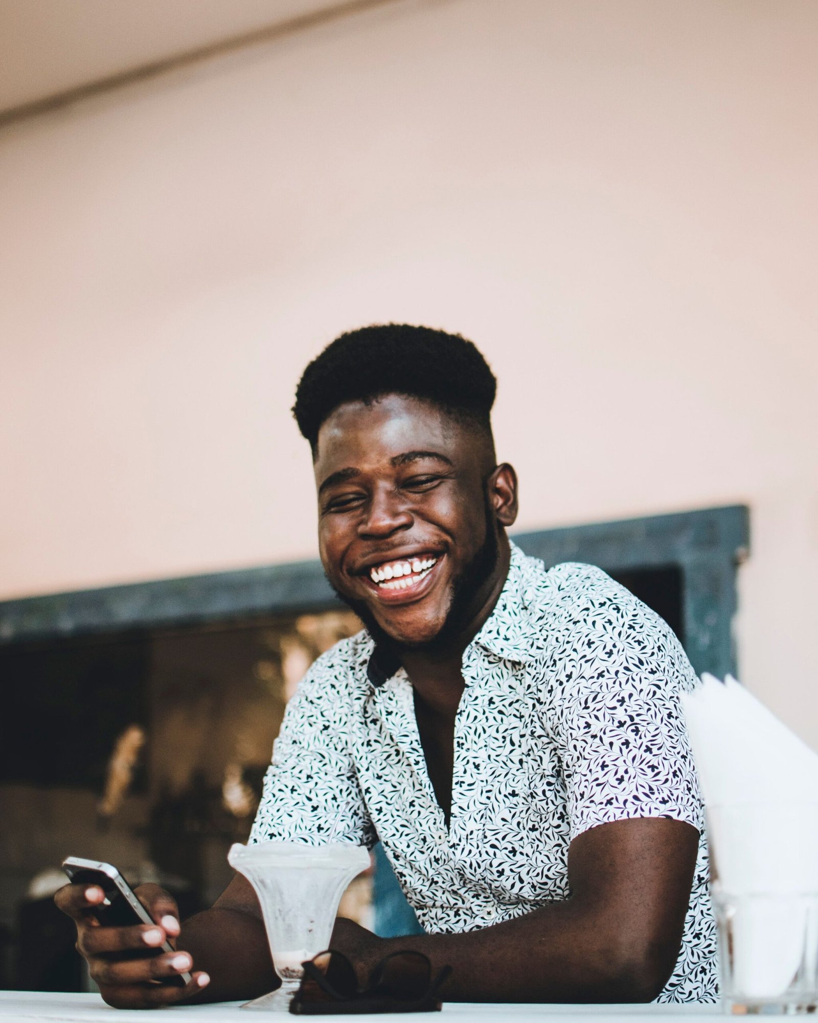 Happy African American man smiling while holding a phone and enjoying coffee indoors.